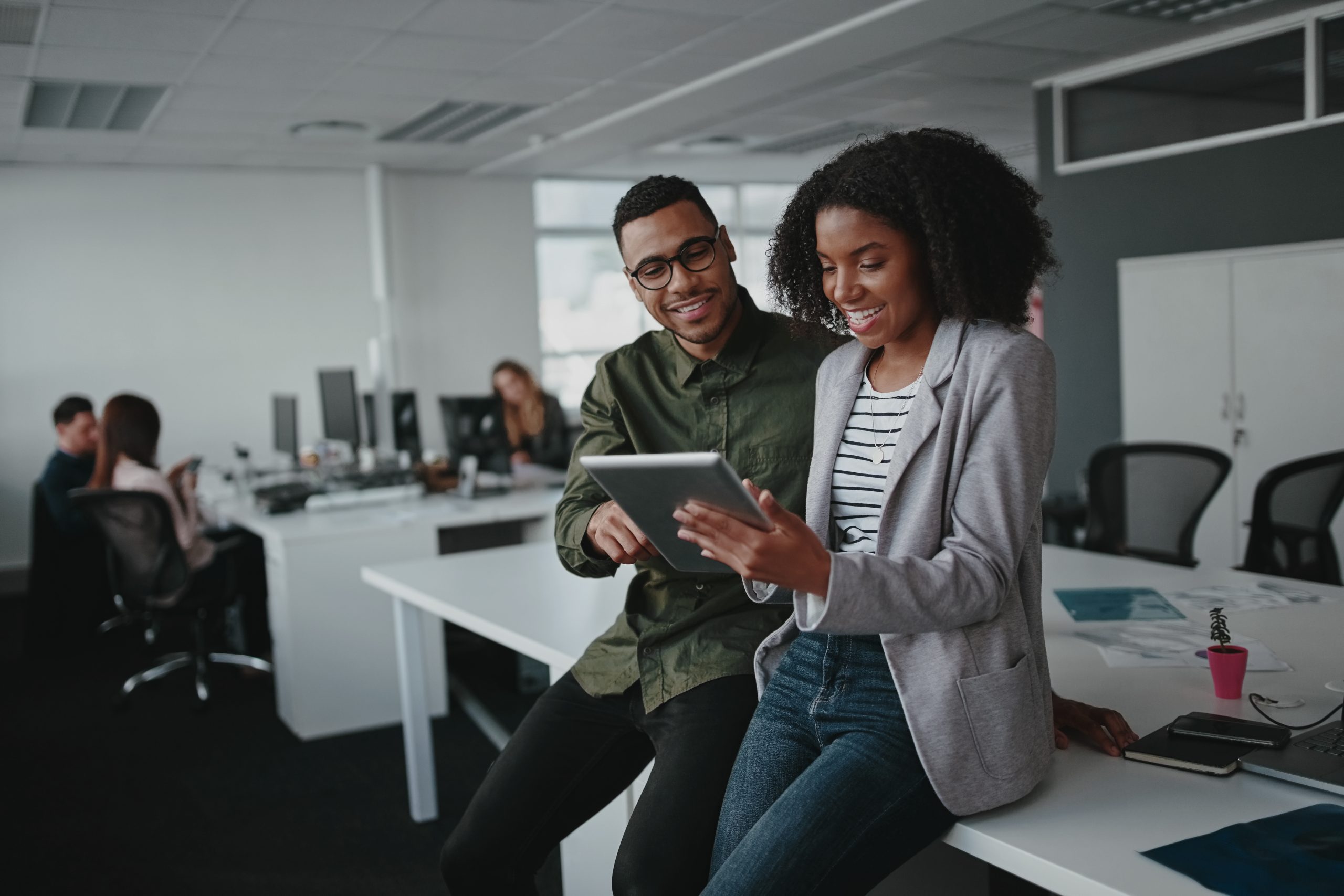 A Black man and a Black woman talking and using digital tablet in an office