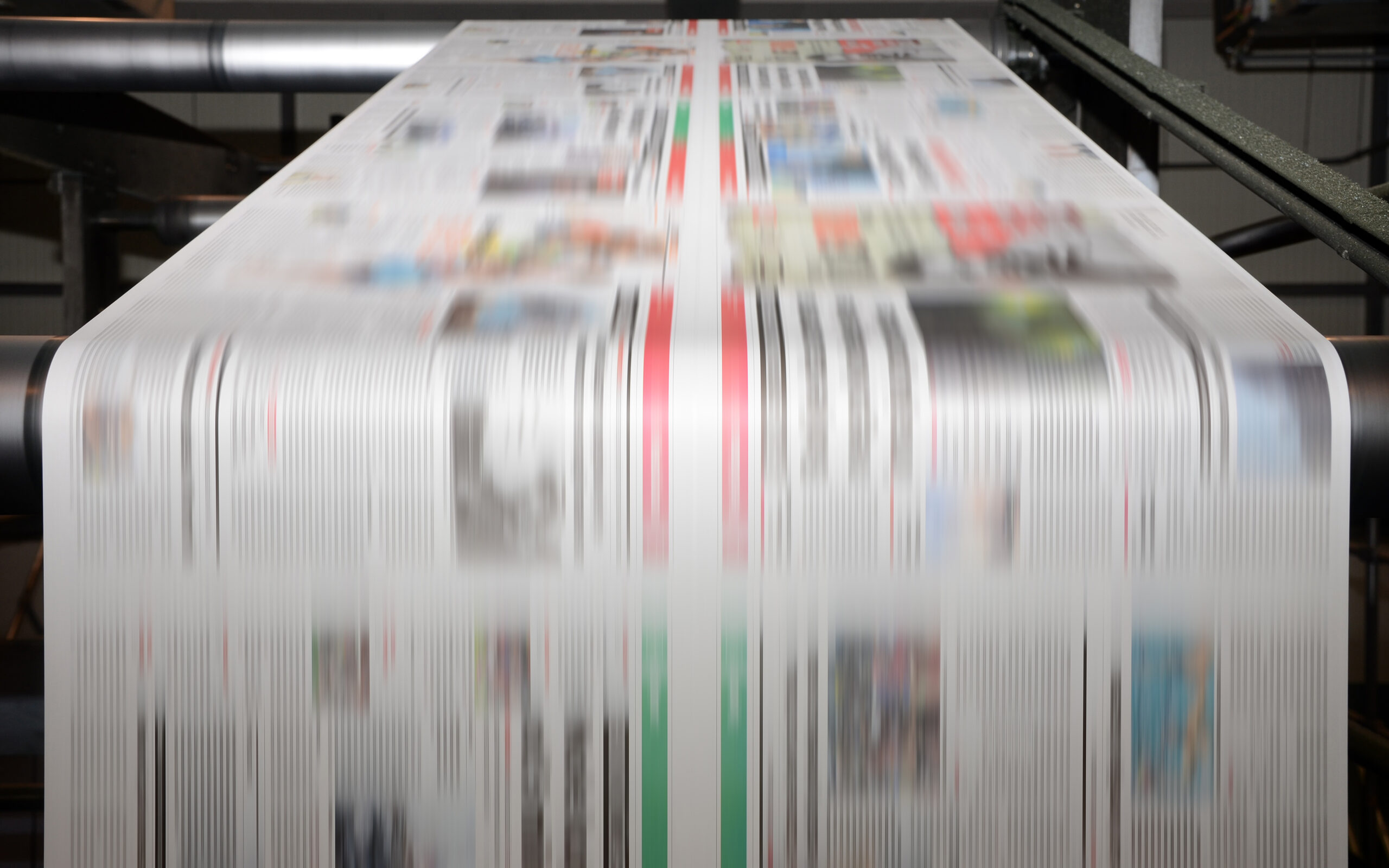 A large offset printing press running a long roll off paper over its rollers at high speed.